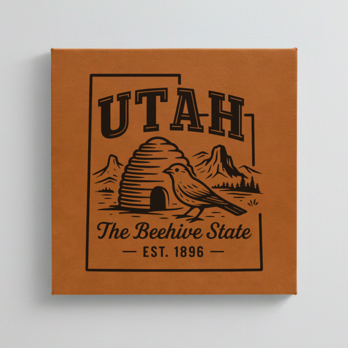 Close up of the Utah design engraved on Brown leatherette: a beehive, a California gull and red rock arches, "The Beehive State", EST. 1896
