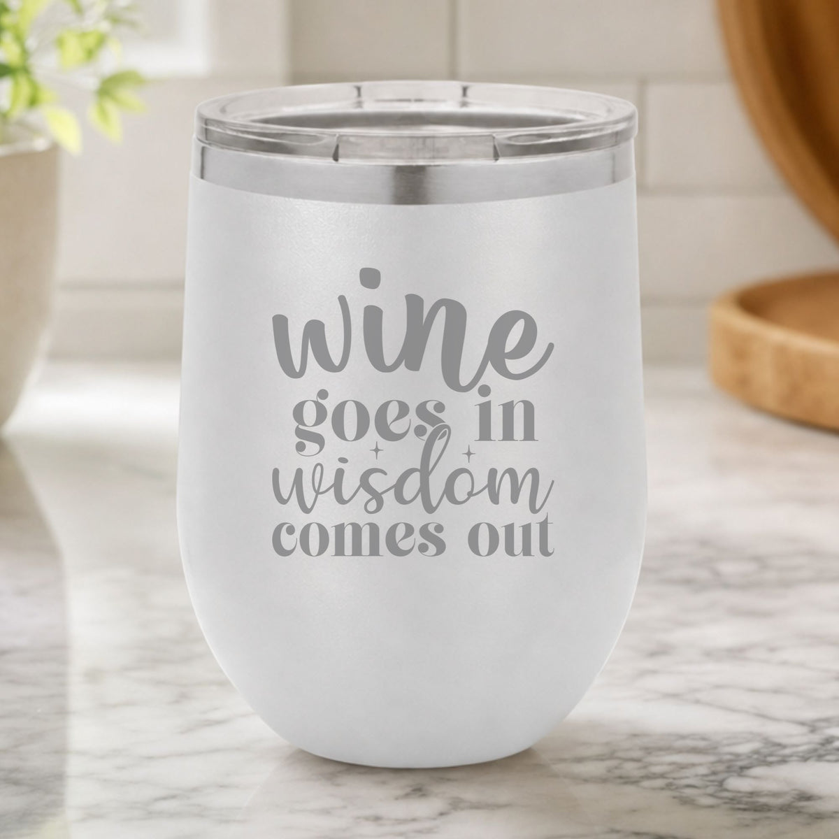 White 12 oz stemless wine tumbler laser engraved with "Wine Goes In, Wisdom Comes Out", on a kitchen counter