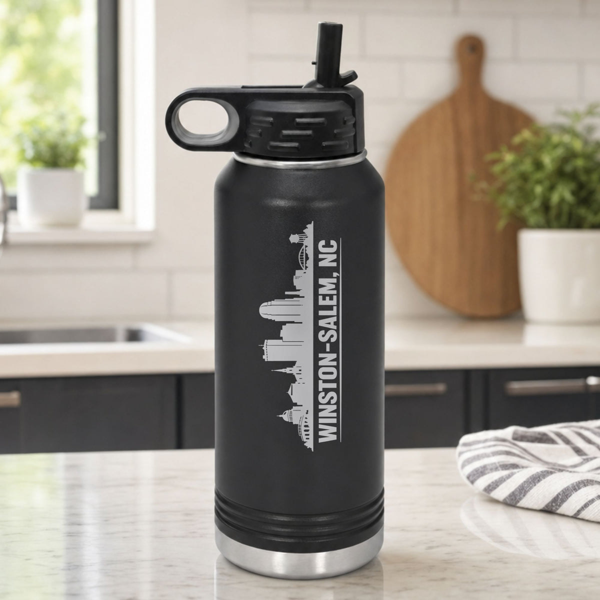 Black 32 oz insulated water bottle laser engraved with the Winston-Salem, North Carolina skyline running up the side, standing on a kitchen counter