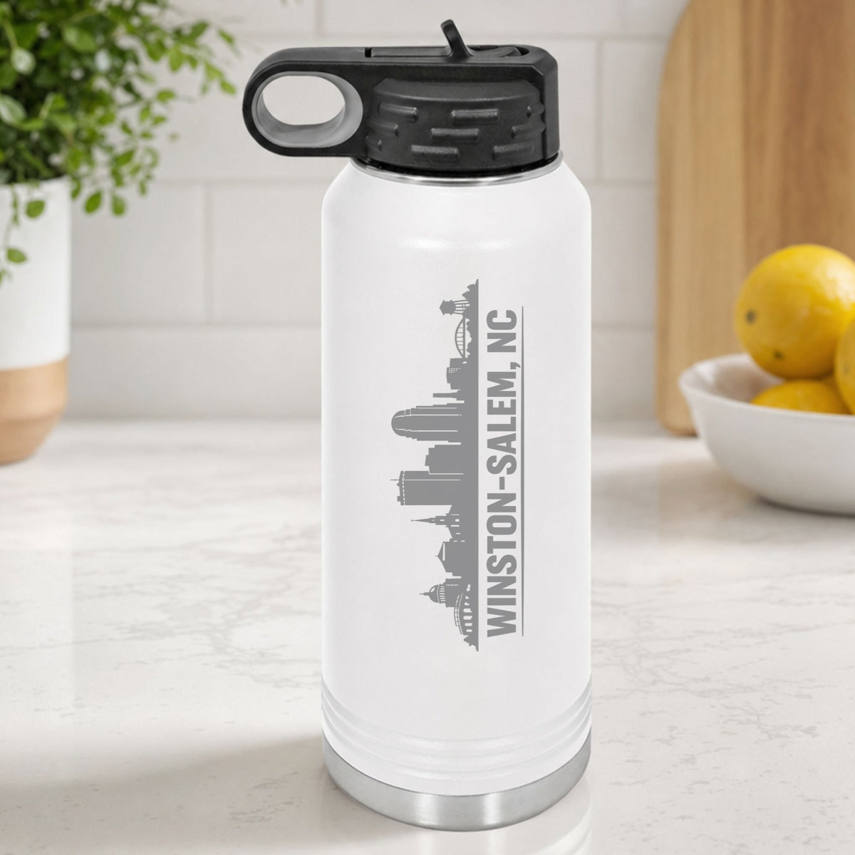 White 32 oz insulated water bottle laser engraved with the Winston-Salem, North Carolina skyline running up the side, standing on a kitchen counter