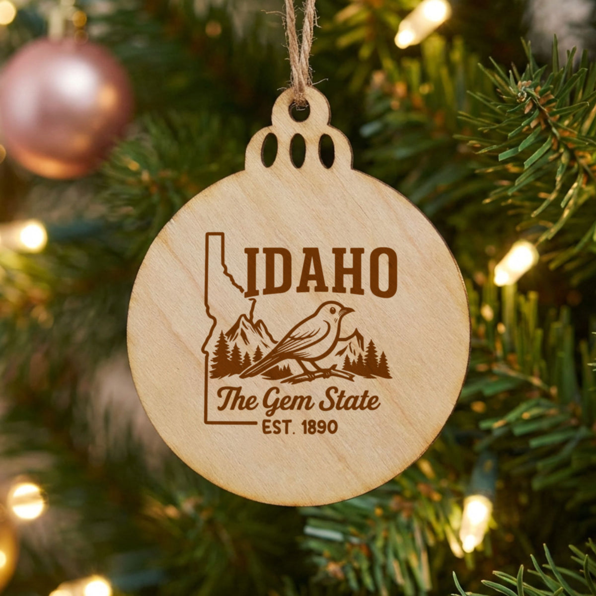 Round wood Christmas ornament laser engraved with an Idaho design of a mountain bluebird, mountains and pines