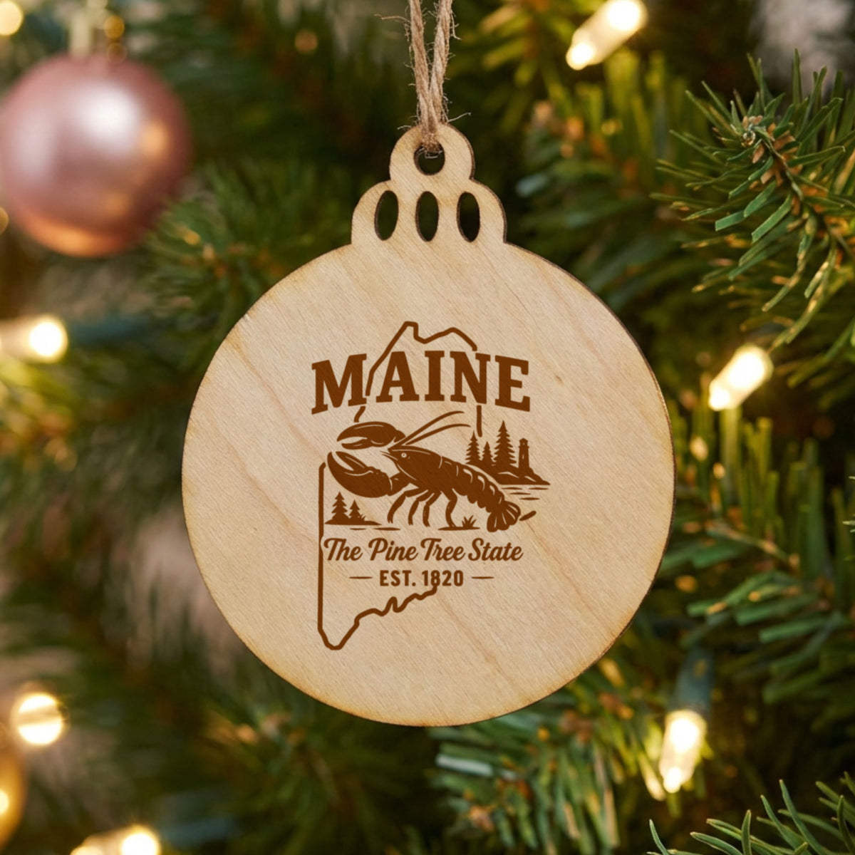 Round wood Christmas ornament laser engraved with a Maine design of a lobster, pines and a lighthouse