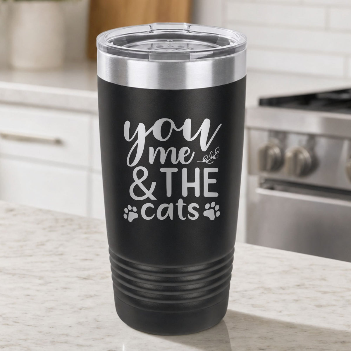 Black 20 oz tumbler laser engraved with "You, Me & the Cats", plus paw prints, on a kitchen counter