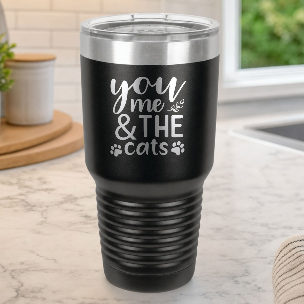 Black 30 oz tumbler laser engraved with "You, Me & the Cats", plus paw prints, on a kitchen counter