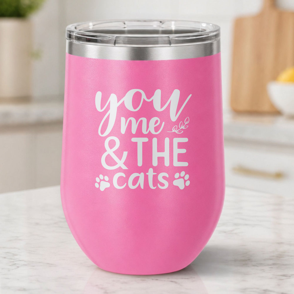 Pink 12 oz stemless wine tumbler laser engraved with "You, Me & the Cats", plus paw prints, on a kitchen counter
