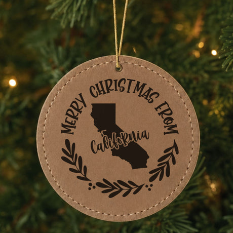 Brown leatherette round Christmas ornament engraved Merry Christmas From California, with the state shape in a laurel wreath, hanging on a tree