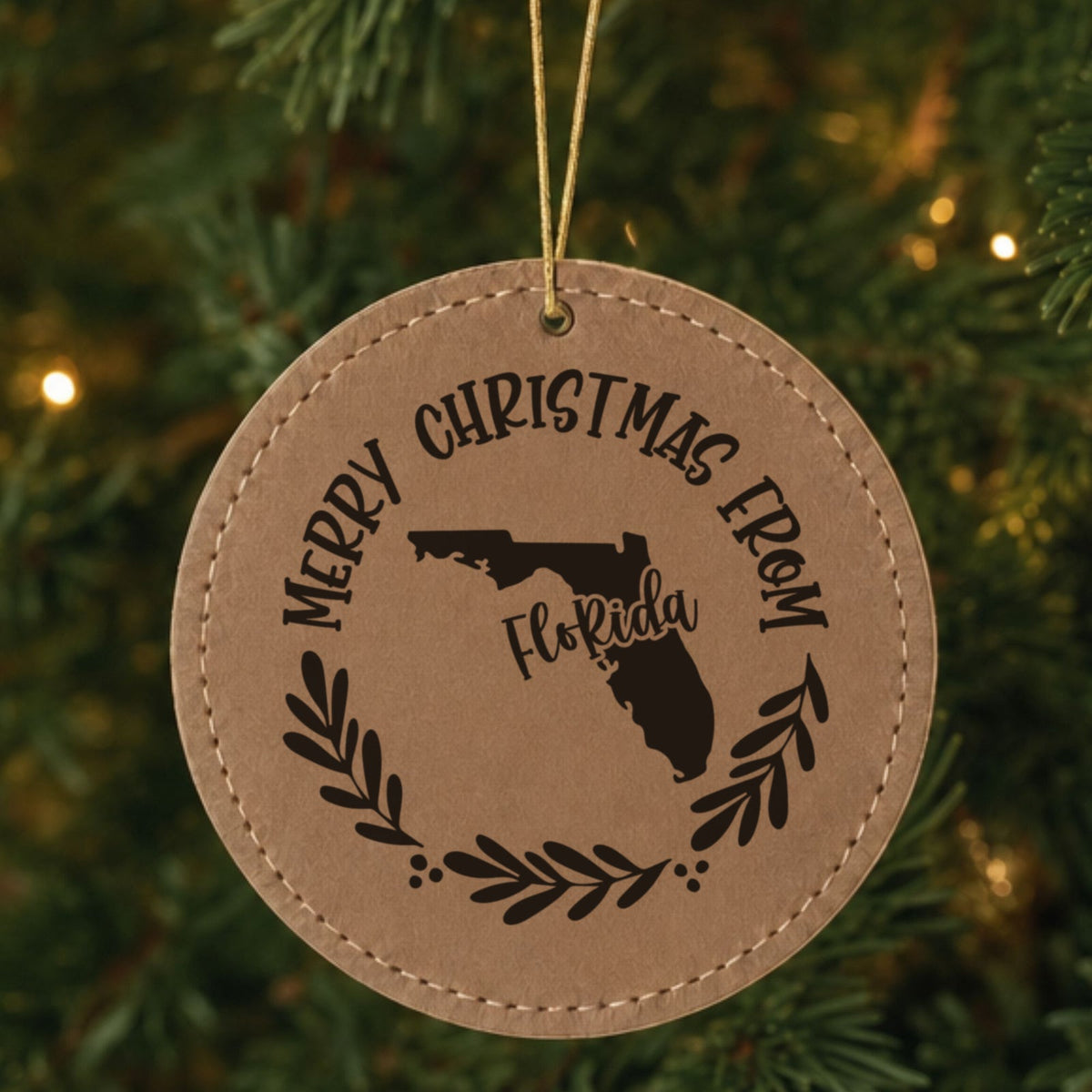Brown leatherette ornament engraved Merry Christmas From Florida with the state shape in a laurel wreath, hanging on a tree