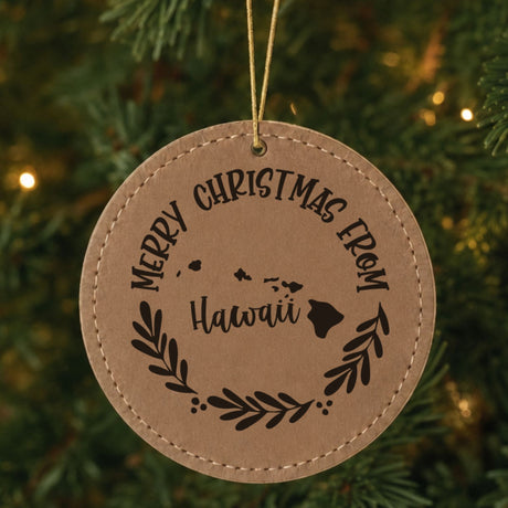 Brown leatherette ornament engraved Merry Christmas From Hawaii with the island chain in a laurel wreath, hanging on a tree