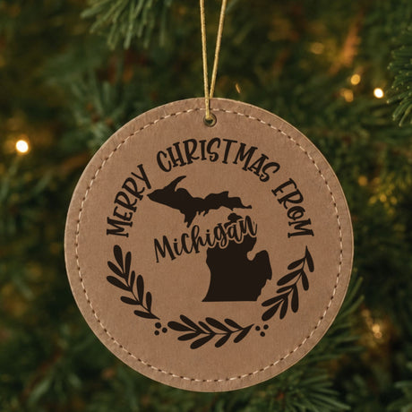 Brown leatherette round Christmas ornament engraved Merry Christmas From Michigan, with the state shape in a laurel wreath, hanging on a tree