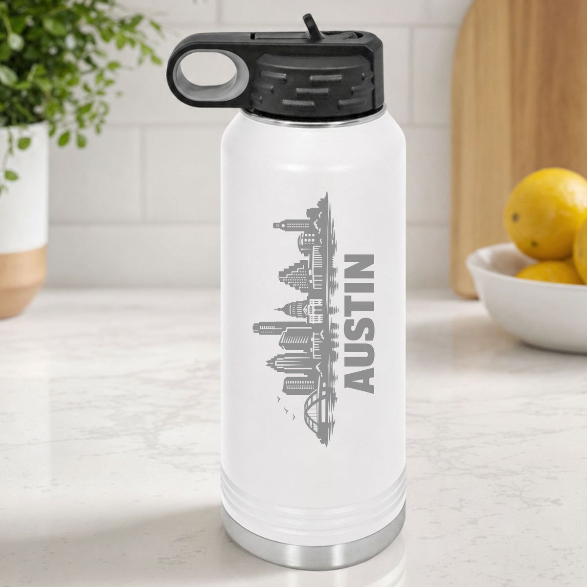 White 32 oz insulated water bottle laser engraved with the Austin, Texas skyline running up the side, standing on a kitchen counter