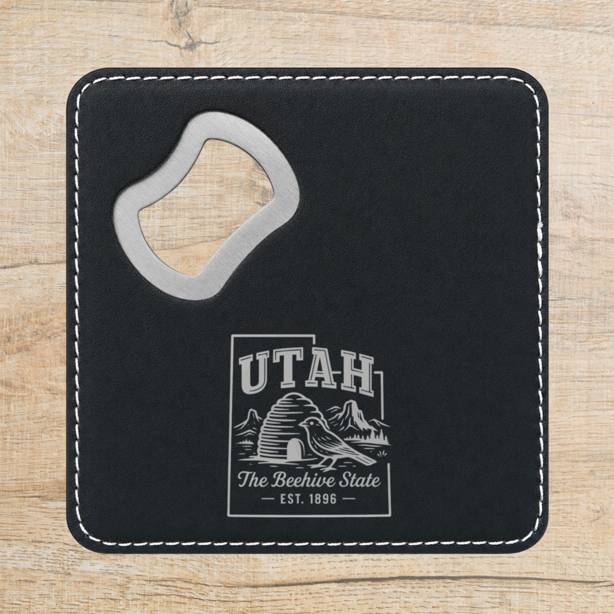 Black leatherette bottle opener coaster laser engraved with a Utah design of a beehive, a California gull and red rock arches