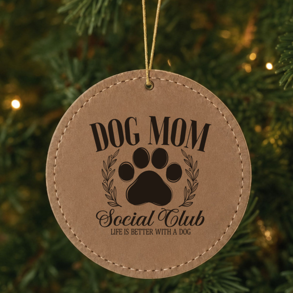 Brown leatherette Christmas ornament engraved with a Dog Mom Social Club crest design with a paw print and laurel wreath