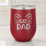 Maroon 12 oz stemless wine tumbler laser engraved with "Cat Dad" framed by cat ears and whiskers, on a kitchen counter