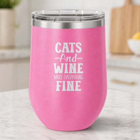Pink 12 oz stemless wine tumbler laser engraved with "Cats and Wine Make Everything Fine", on a kitchen counter