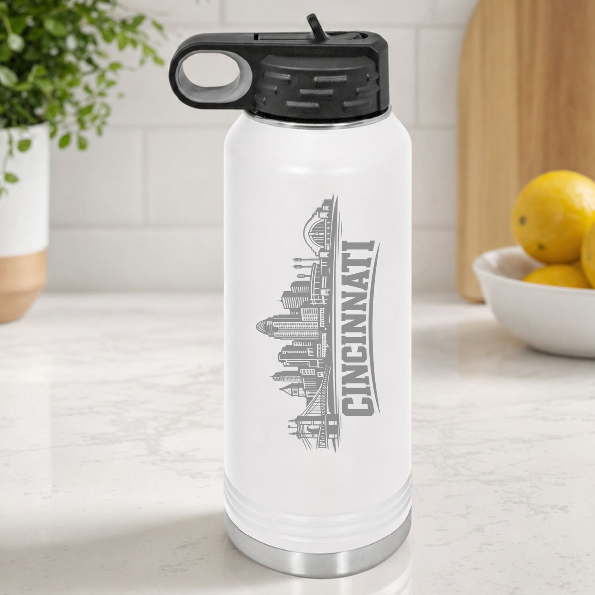 White 32 oz insulated water bottle laser engraved with the Cincinnati, Ohio skyline running up the side, standing on a kitchen counter