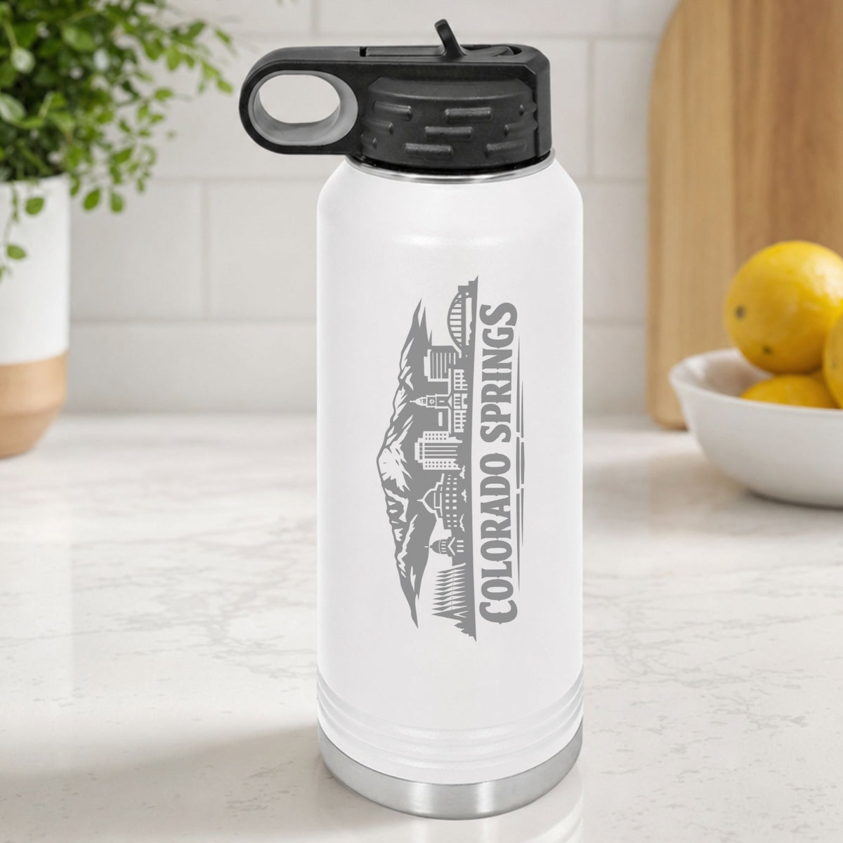 White 32 oz insulated water bottle laser engraved with the Colorado Springs, Colorado skyline running up the side, standing on a kitchen counter