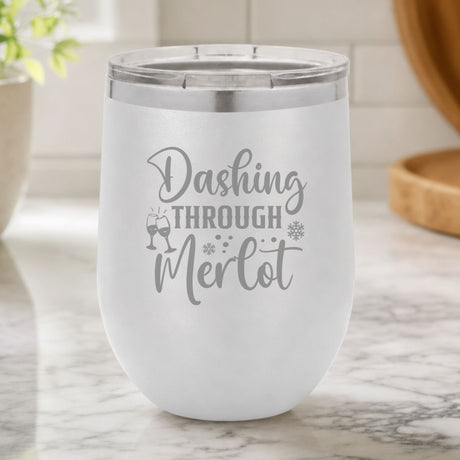 White 12 oz stemless wine tumbler laser engraved with "Dashing Through Merlot", on a kitchen counter