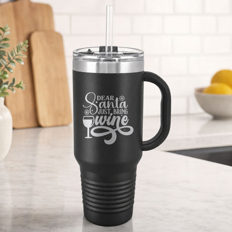 Black 40 oz tumbler with handle and straw laser engraved with "Dear Santa, Just Bring Wine", on a kitchen counter