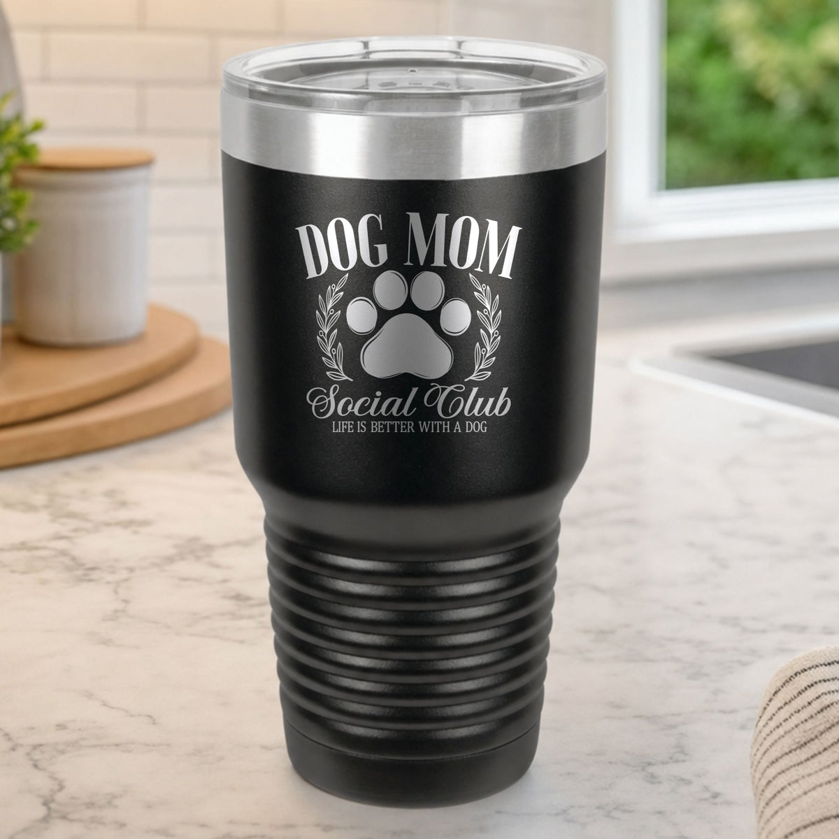 Black 30 oz tumbler laser engraved with the Social Club "Dog Mom" design, on a kitchen counter