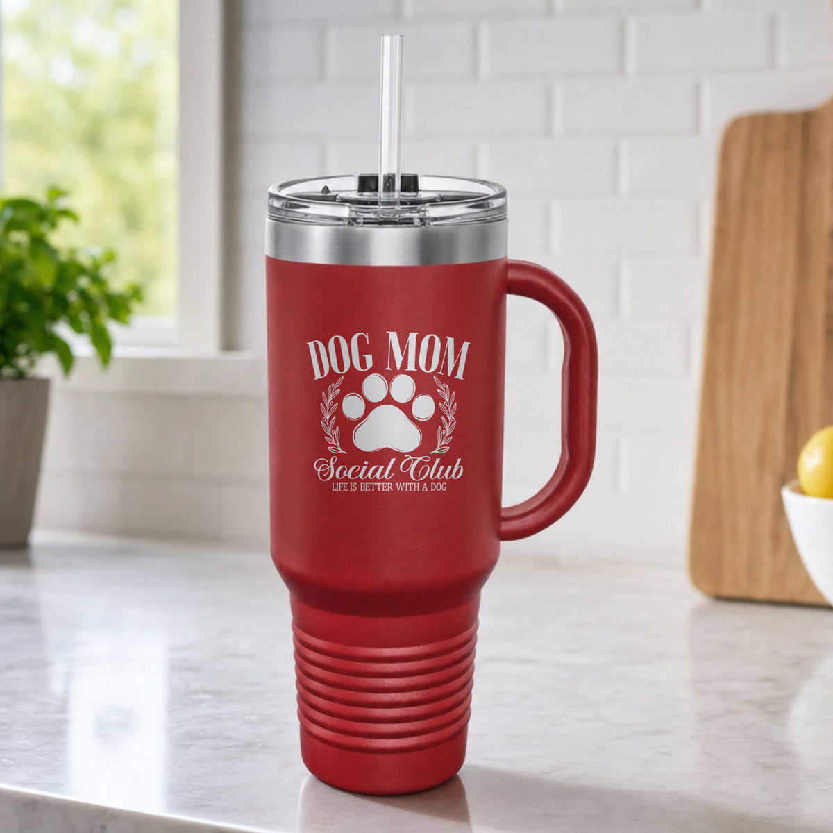 Maroon 40 oz tumbler with handle and straw laser engraved with the Social Club "Dog Mom" design, on a kitchen counter