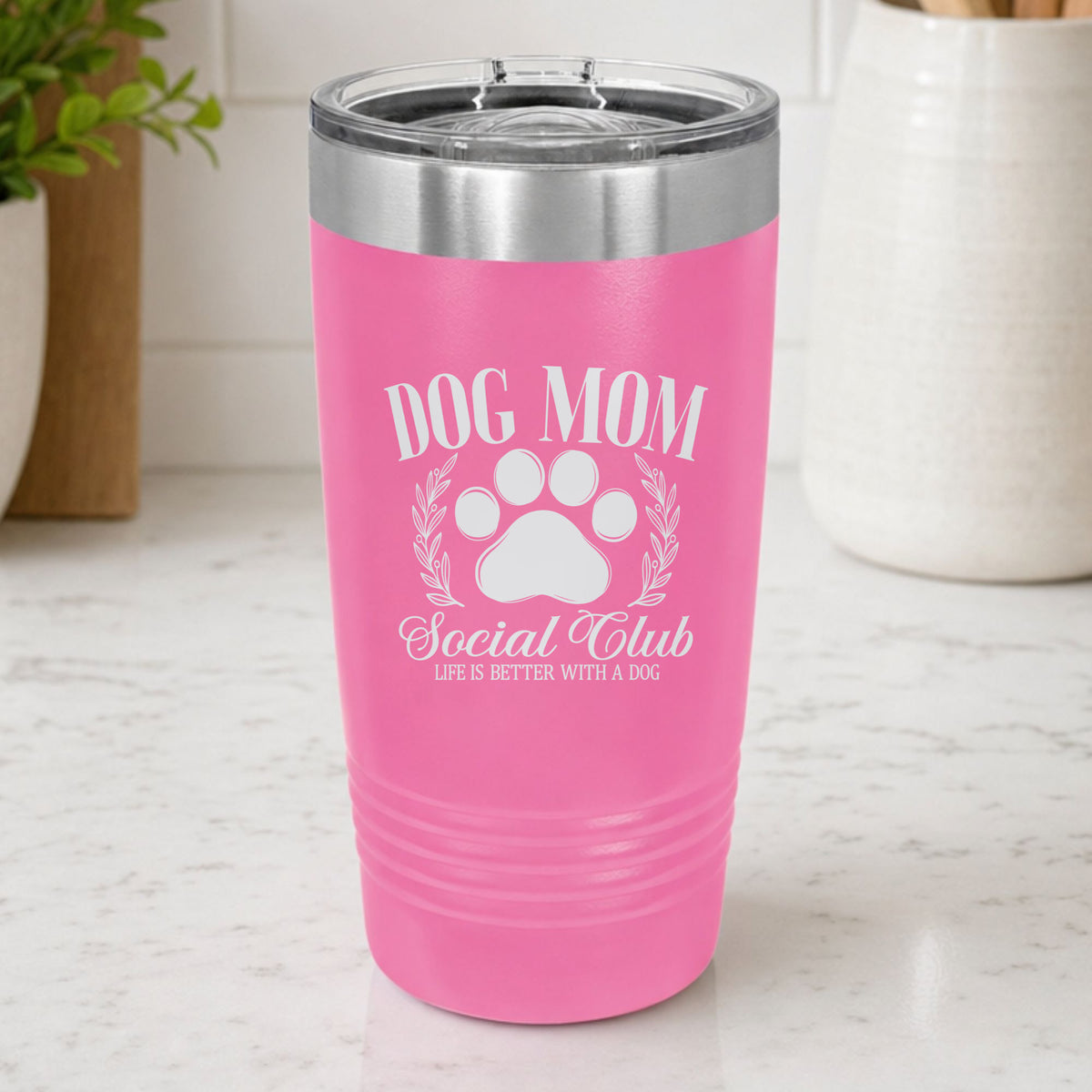 Pink 20 oz tumbler laser engraved with the Social Club "Dog Mom" design, on a kitchen counter