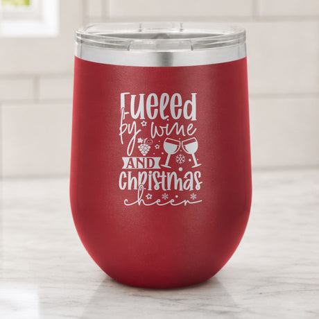Maroon 12 oz stemless wine tumbler laser engraved with "Fueled by Wine and Christmas Cheer", on a kitchen counter