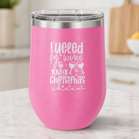 Pink 12 oz stemless wine tumbler laser engraved with "Fueled by Wine and Christmas Cheer", on a kitchen counter