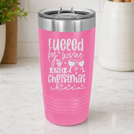 Pink 20 oz tumbler laser engraved with "Fueled by Wine and Christmas Cheer", on a kitchen counter