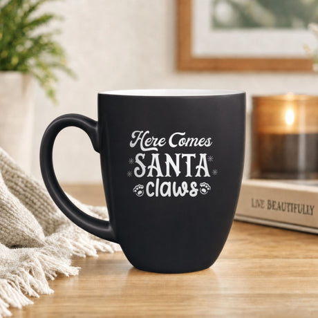16 oz black ceramic coffee mug with "Here Comes Santa Claws"