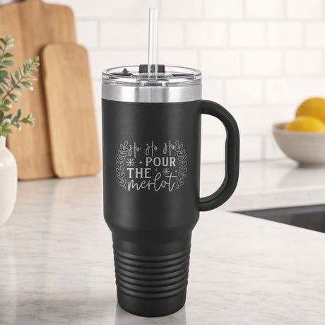 Black 40 oz tumbler with handle and straw laser engraved with "Ho Ho Ho, Pour the Merlot", on a kitchen counter