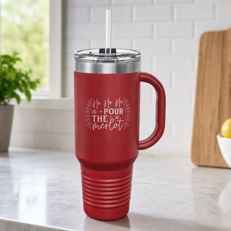 Maroon 40 oz tumbler with handle and straw laser engraved with "Ho Ho Ho, Pour the Merlot", on a kitchen counter
