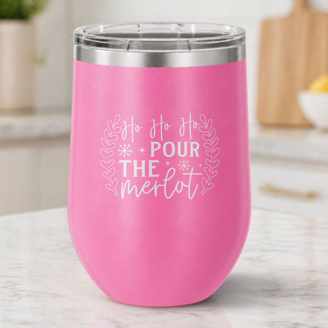 Pink 12 oz stemless wine tumbler laser engraved with "Ho Ho Ho, Pour the Merlot", on a kitchen counter