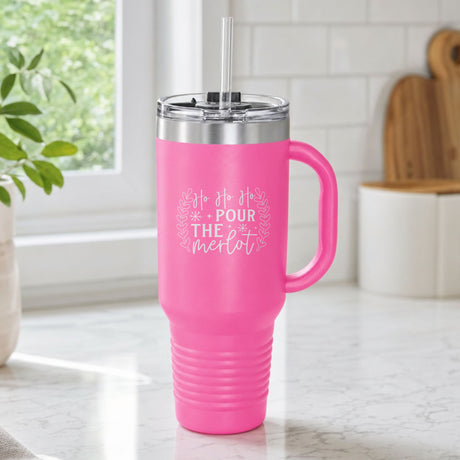 Pink 40 oz tumbler with handle and straw laser engraved with "Ho Ho Ho, Pour the Merlot", on a kitchen counter