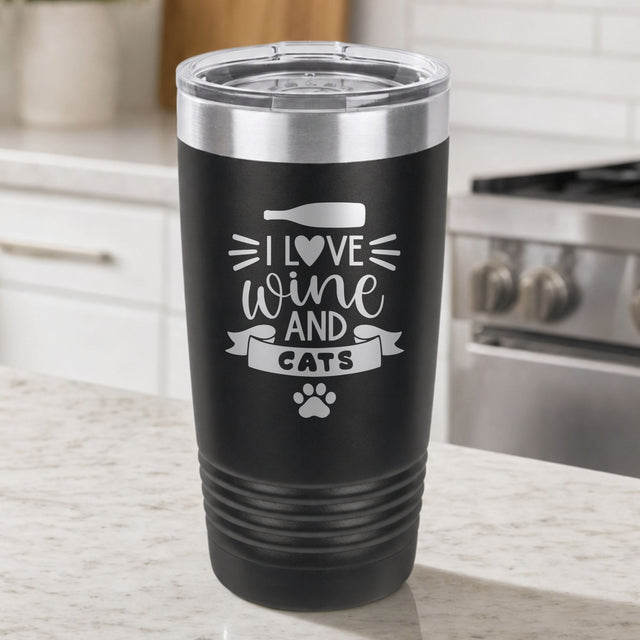 Black 20 oz tumbler laser engraved with "I Love Wine and Cats", a wine bottle, a heart and a paw print, on a kitchen counter