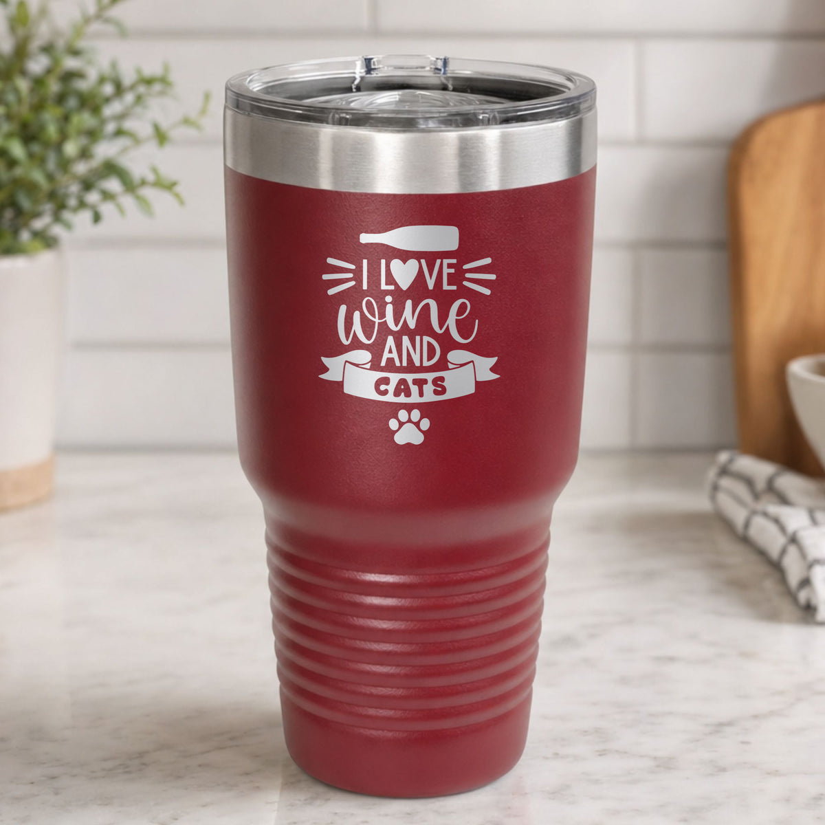 Maroon 30 oz tumbler laser engraved with "I Love Wine and Cats", a wine bottle, a heart and a paw print, on a kitchen counter