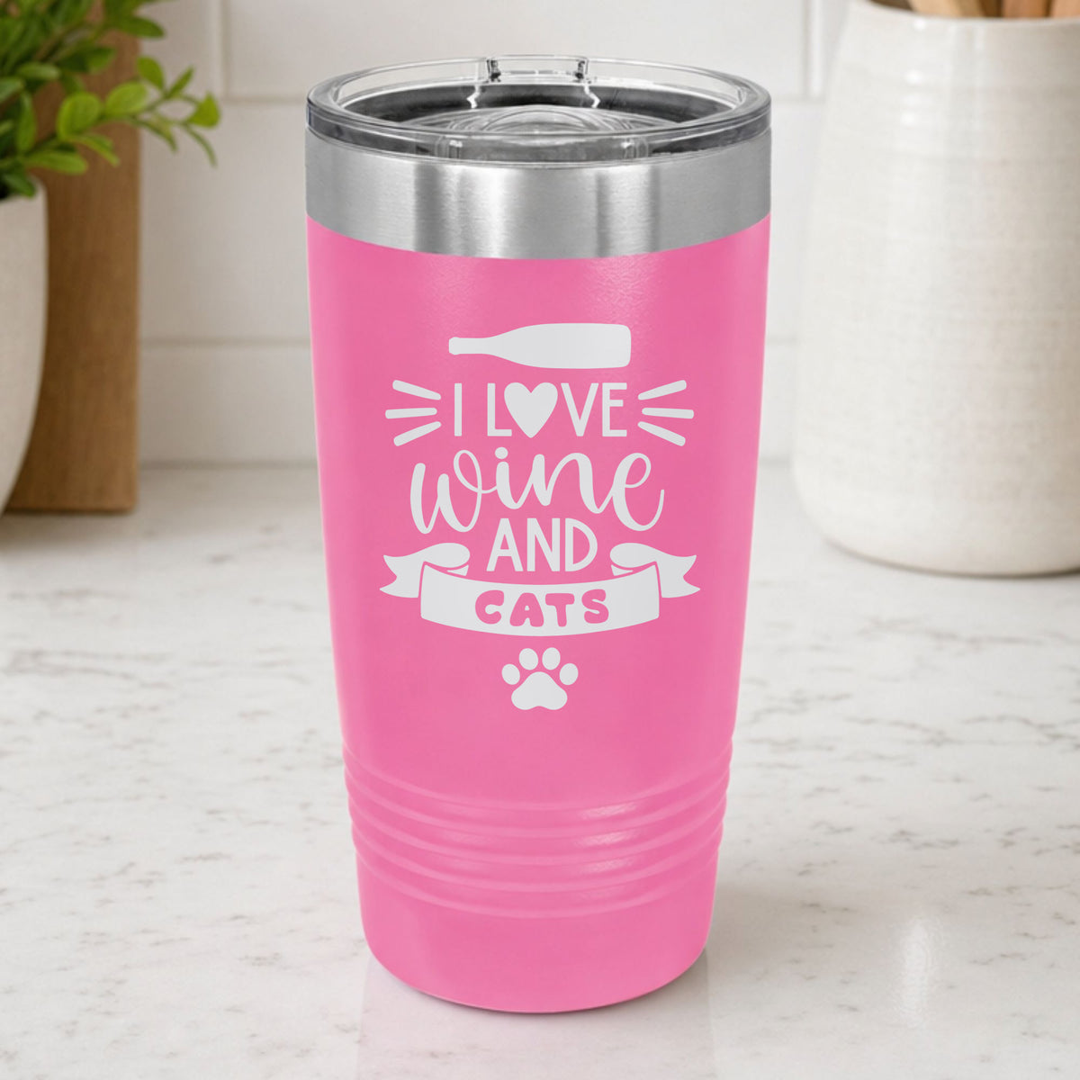 Pink 20 oz tumbler laser engraved with "I Love Wine and Cats", a wine bottle, a heart and a paw print, on a kitchen counter
