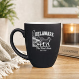 Black 16 oz ceramic coffee mug printed with the Delaware state outline and The First State