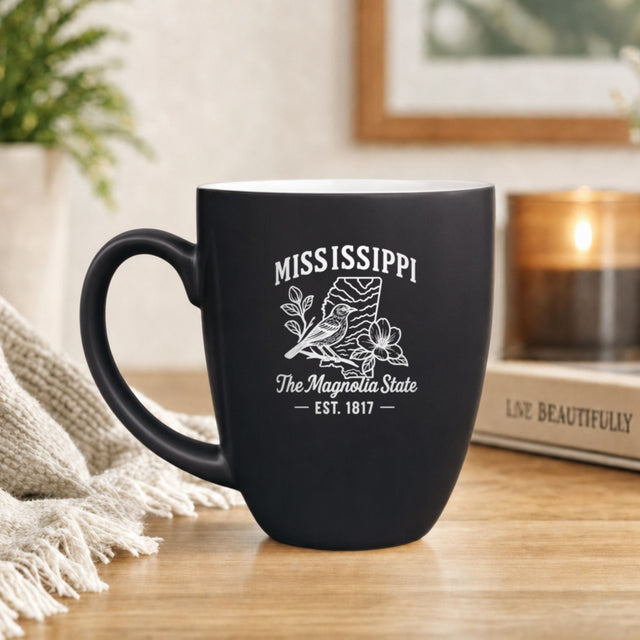 Black 16 oz ceramic coffee mug printed with the Mississippi state outline and The Magnolia State