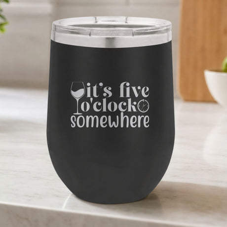 Black 12 oz stemless wine tumbler laser engraved with "It's Five O'Clock Somewhere", on a kitchen counter