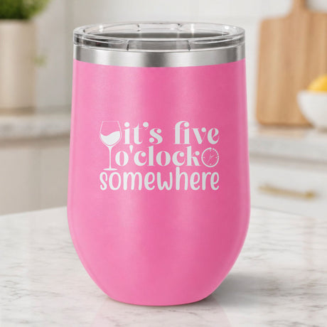 Pink 12 oz stemless wine tumbler laser engraved with "It's Five O'Clock Somewhere", on a kitchen counter