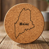Maine round cork coaster engraved with the state outline and MAINE in hand-drawn brush lettering