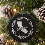 Black leatherette round Christmas ornament engraved Merry Christmas From California, with the state shape in a laurel wreath, hanging on a tree