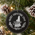 Black leatherette round Christmas ornament engraved Merry Christmas From New Hampshire, with the state shape in a laurel wreath, hanging on a tree