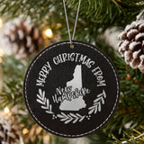 Black leatherette round Christmas ornament engraved Merry Christmas From New Hampshire, with the state shape in a laurel wreath, hanging on a tree