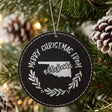 Black leatherette round Christmas ornament engraved Merry Christmas From Oklahoma, with the state shape in a laurel wreath, hanging on a tree