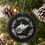 Black leatherette round Christmas ornament engraved Merry Christmas From West Virginia, with the state shape in a laurel wreath, hanging on a tree