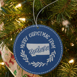 Blue leatherette round Christmas ornament engraved Merry Christmas From Montana, with the state shape in a laurel wreath, hanging on a tree