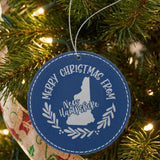 Blue leatherette round Christmas ornament engraved Merry Christmas From New Hampshire, with the state shape in a laurel wreath, hanging on a tree