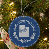 Blue leatherette round Christmas ornament engraved Merry Christmas From Utah, with the state shape in a laurel wreath, hanging on a tree