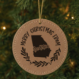 Brown leatherette round Christmas ornament engraved Merry Christmas From Georgia, with the state shape in a laurel wreath, hanging on a tree